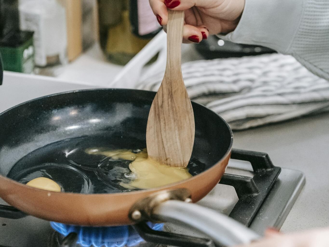 A person cooking eggs in a pan with a wooden spatula on a kitchen stove.